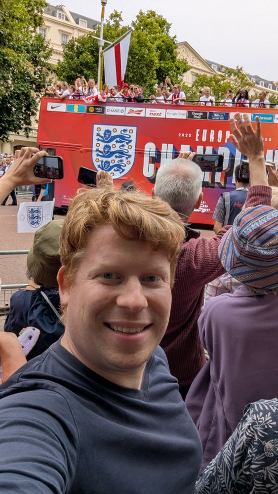 Paul smiling with red Lionesses bus behind him and fans waving.