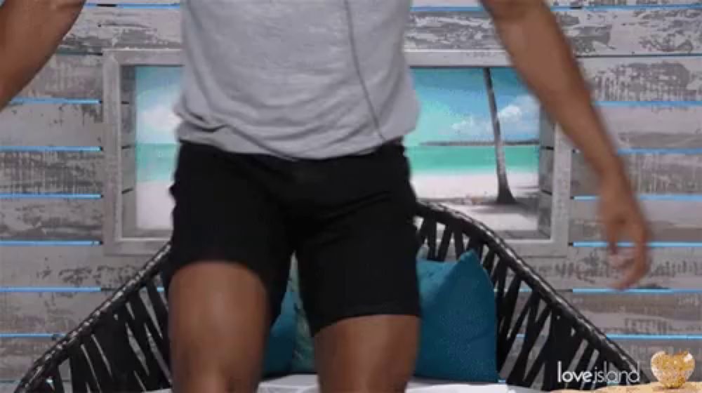 a man in a grey shirt and black shorts is sitting on a love island couch .