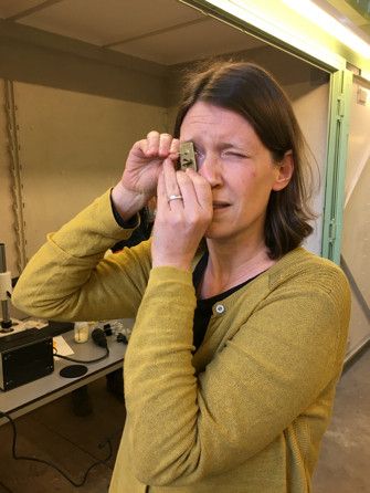 Sietske Fransen kijkt naar vloeistof in een heel dun glazen buisje, door een replica Leeuwenhoekmicroscoop. Ik moet de microscoop heel dicht tegen mijn oog houden om überhaupt iets te kunnen. 