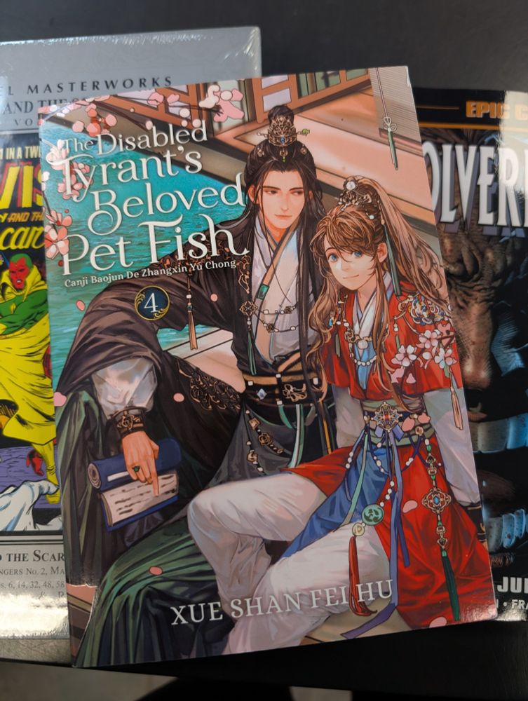 Pile of books with danmei title The Disabled Tyrant's Beloved Pet Fish volume 4 on top of a Marvel masterwork and epic collection