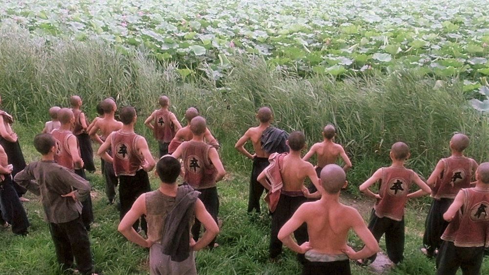 A group of boys standing in a field facing away from the camera, singing and practicing 