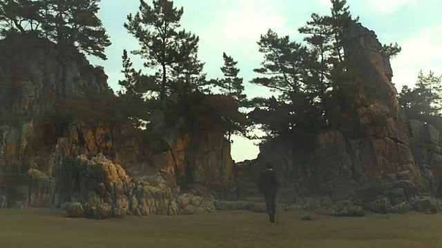 Jang Hae-jun walking up to a cliff that connects to a beach