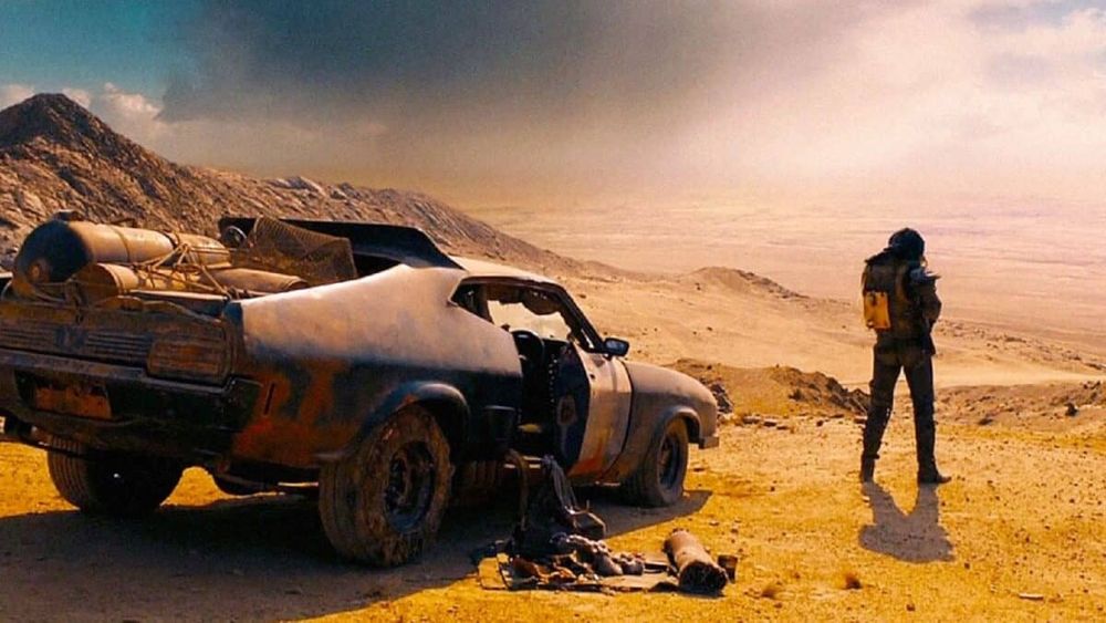 Max stands by his car in a desert