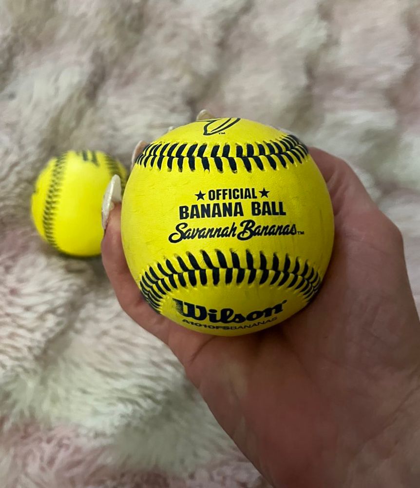 Hand holding yellow baseball that reads: ⭐️ OFFICIAL ⭐️ Banana Ball Savannah Bananas 
