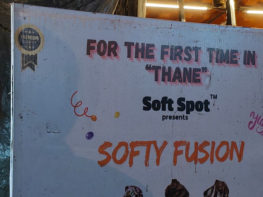 A sign outside a shop that says:

For the first time in
“Thane”
Soft Spot™
Presents
Softy Fusion