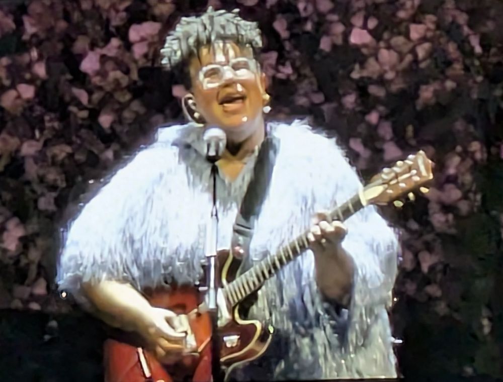 Brittany Howard in a big white dress, playing guitar and singing 