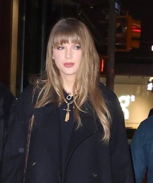 taylor swift walking and heading a black coat with a gold necklace 
