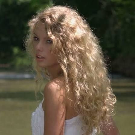 taylor swift during debut photoshoot. she's looking over her shoulder, and her hair is curly, and she's wearing a white dress 