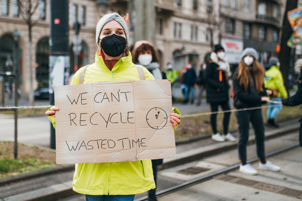 Demonstrator with a sign that reads "We can't recycle wasted time" at a protest against climate change, photo credit: Ivan Radic, CC BY 2.0 <https://creativecommons.org/licenses/by/2.0>, via Wikimedia Commons
