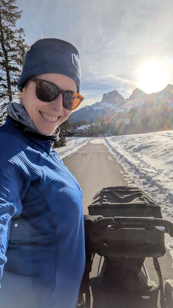 A woman in a blue sweater pushing a stroller with mountains in the background