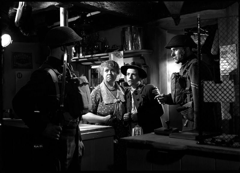 Two women in 1940s clothes stand close while surrounded by two threatening figures wearing British WW2 uniforms. These are all stills from the 1942 Cavalcanti film, Went The Day Well. 