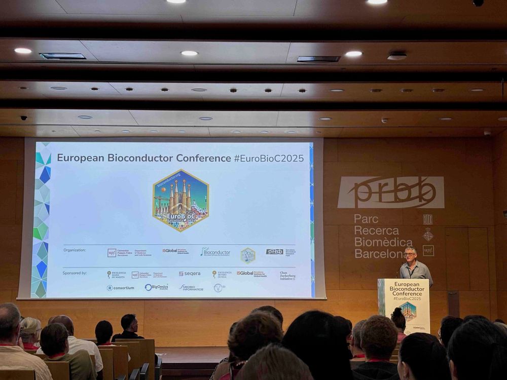 EuroBioC2025 welcome in PRBB auditorium by host Robert Castelo, showing slides with conference sticker and sponsor logos.
