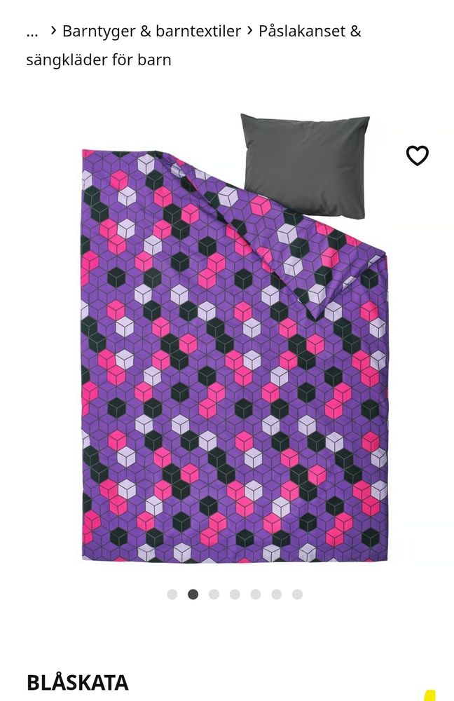 A imagem mostra um conjunto de roupa de cama infantil da coleção BLÅSKATA. O edredom tem um padrão geométrico vibrante composto por cubos tridimensionais em cores roxas, pretas, rosas e brancas sobre um fundo roxo. A fronha é de cor cinza escura, lisa, sem estampas. O design é moderno, lúdico e chamativo, ideal para um quarto infantil com um toque divertido e criativo. O texto está em sueco e indica que se trata de um item da seção de tecidos e roupas de cama para crianças.
