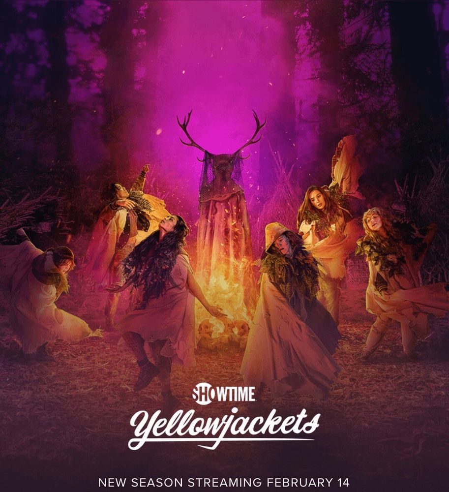 a group of young women are dressed in gowns dancing in a circle around a fire. merging in the fire above is a hooded figure with antlers and we cannot see their face. the background is a forest at night with pink smoke emanating as well. at the bottom it reads “showtime yellowjackets - new season streaming February 14”