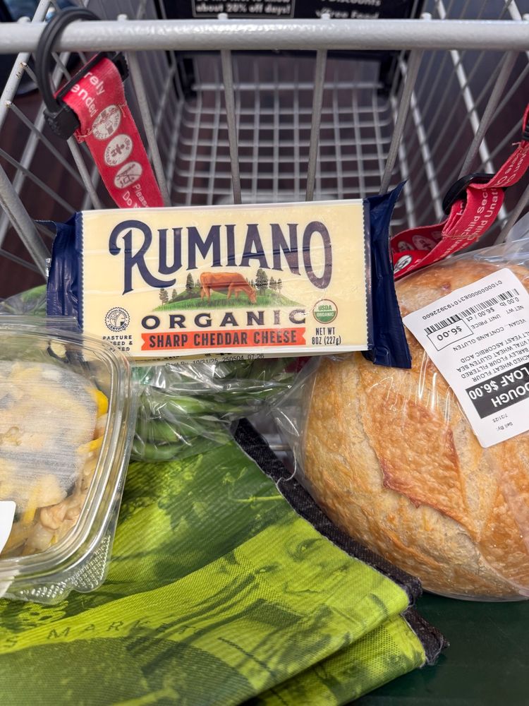 Rumiano brand sharp cheddar cheese in a shopping cart next to a loaf of sourdough bread. 