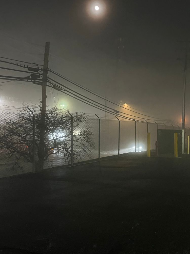 A street view image of an insanely foggy night in Cincinnati, OH. The fog is so hazy that you can barely see the other side of the street, and you can only make out cars by their headlights. 