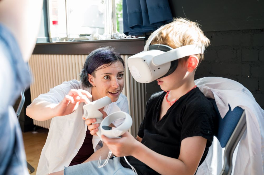 A child wearing a VR headset, with a member of staff explaining how it works 
