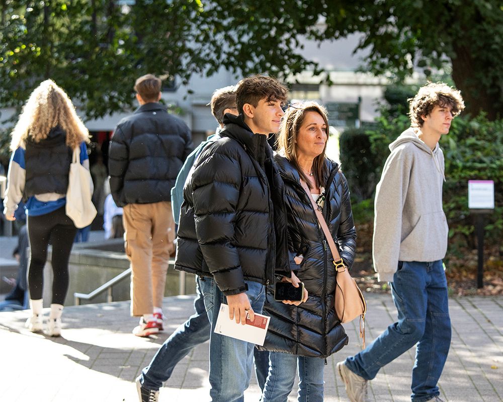 Two people stood near Beech Grove Plaza, University of Leeds. One of them is holding an Open Day booklet in their hand.