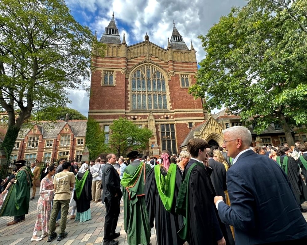 A crowd of people dressed smartly and in graduation gowns stood in front of The Great Hall.
 
