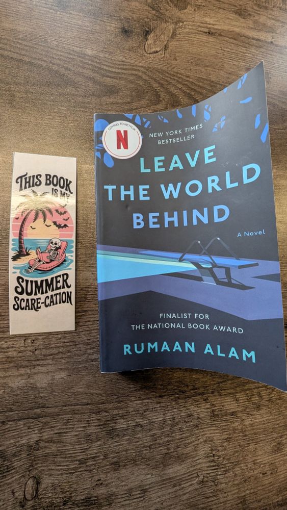 A bookmark lays next to a paperback version of "Leave the world behind" by Rumaan Alam