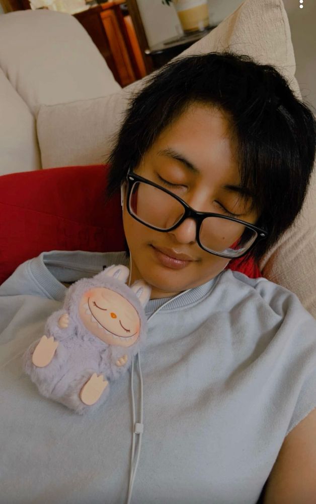 picture of me laying on the couch with my eyes closed, a labubu laying on my chest with her eyes closed