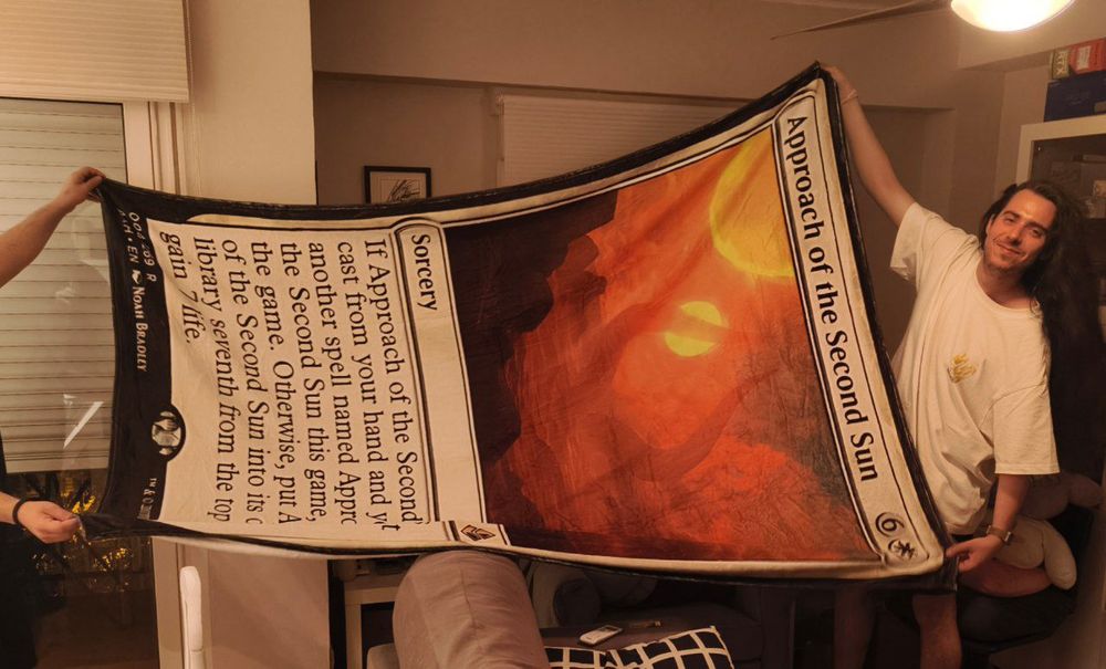 My friend Victor holding a blanket in the shape of the Magic the Gathering card Approach of the Second Sun 