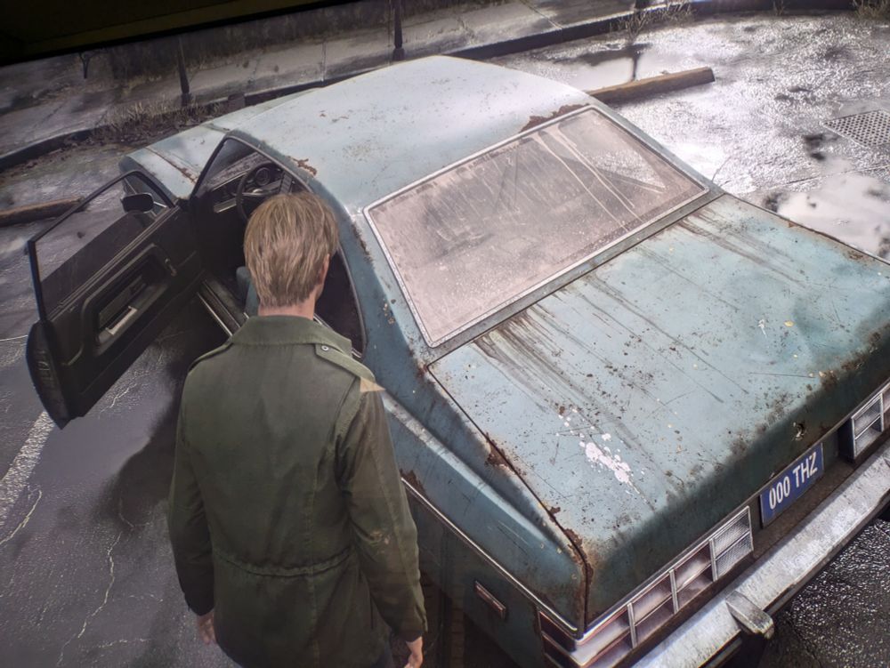 A picture from my TV (lol) playing Silent Hill 2 Remake. It shows James in front of the blue old car at the beginning of the game, where you find the map.