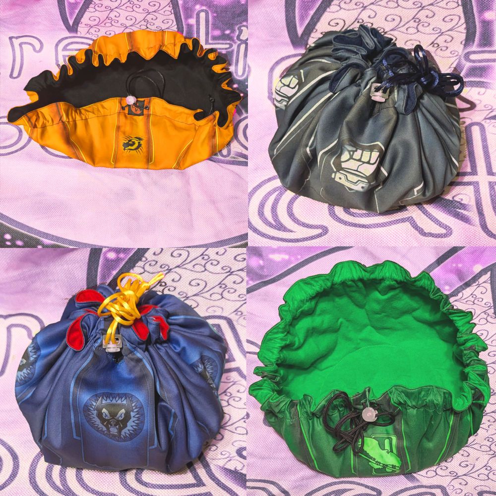 4 separate battletech themed dice bags. orange clan wolverine outer print with a black interior. dark blue house steiner print with a dark blue interior. blue nova cat print with a red interior and gold drawstring. green jade falcon print with emerald green interior and black drawstring.
