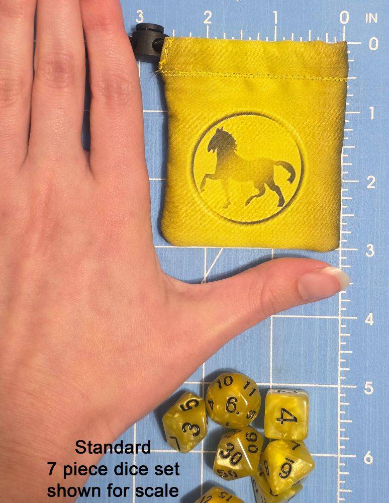 a woman's hand next to a small yellow fabric pouch featuring the Eridani Light Horse faction from the tabletop game Battletech. There is a mat with measurements underneath the hand and pouch, showing the pouch to be 3 inches tall by 2 and a half inches wide. a set of 7 pearlescent yellow dice with black numbers sits near the hand to show further size reference for the pouch.