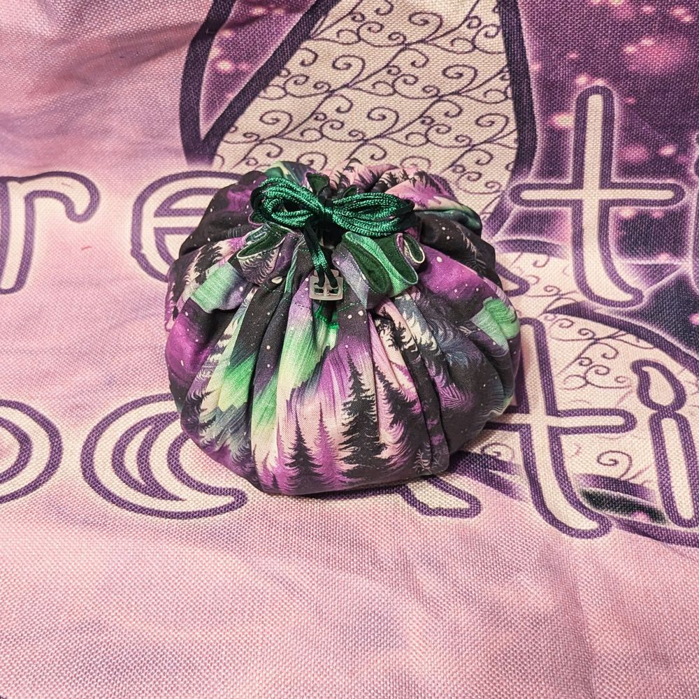 a drawstring bag made of purple and green fabric with an aurora borealis above a forest print.