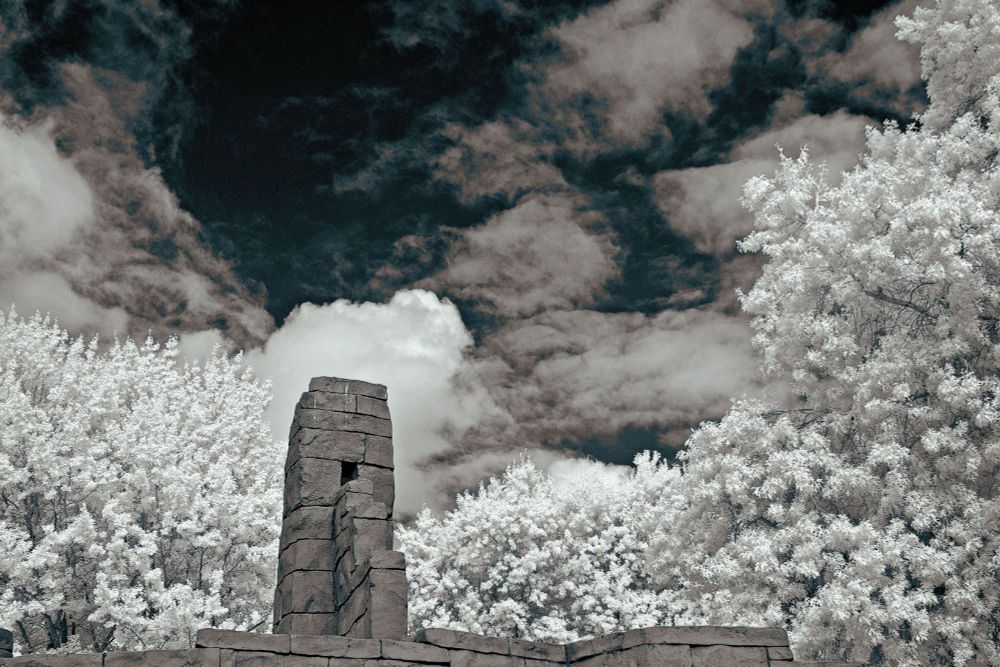 Infrared photograph of a brick sculpture against a background of a clouded black sky and rushes of white leafed trees
