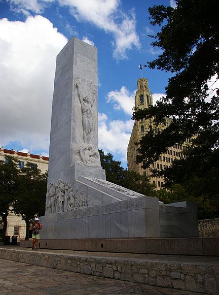 Marble 60-feet tall monument with a wide rectangular base. The second level has carvings of men in 1800s dress at the bottom of a tall rectangular marble piece with a sloping side to meet the corner of the bottom rectangular base. Names carved around the top edge of base of people at the Alamo in 1836. The tall piece has a carving of a semi-nude man reaching towards the sky. The sloping part has some sort of rod with long leaves on each side.