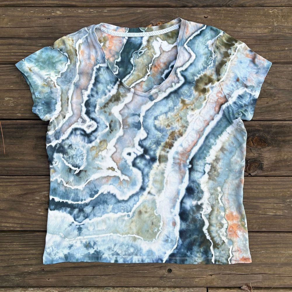 A cotton shirt dyed in shades of blue, olive green, gray, and hints of peach. The dye has a watercolor effect across the shirt.
