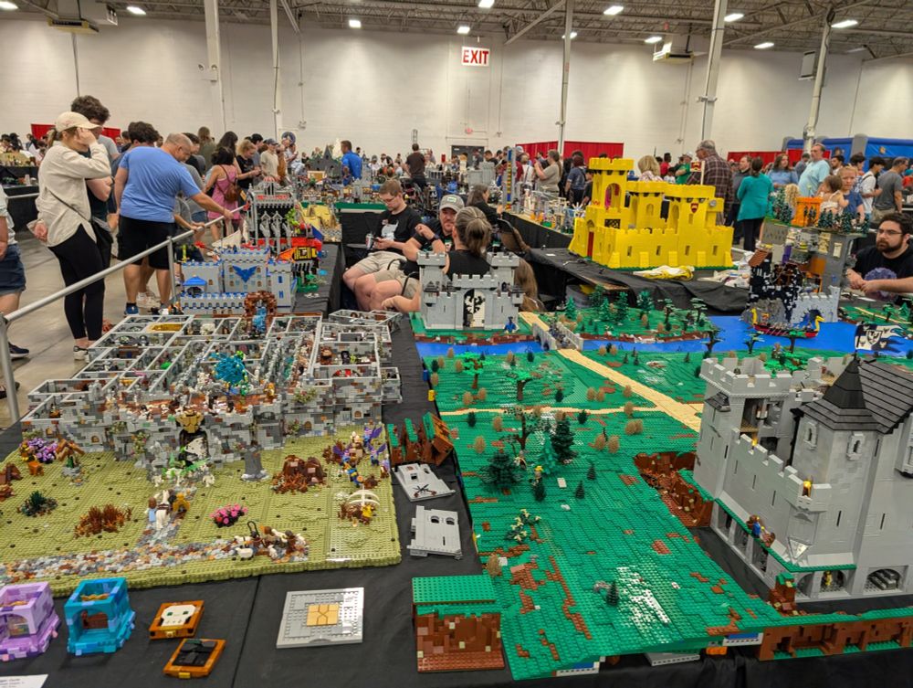 View of several tables at Lego Brickfair 2025 in Chantilly, Virginia on August 3, 2025. The yellow castle in the rear right is especially amazing—it's made out of Lego elements, and is a recreation of a very old-style Lego castle (some of the very earliest Lego castles were yellow) but it's cleverly done in such a way that it *looks* like it's made out of Duplo pieces. Basically, it's like a 4x model of a normal Lego castle.