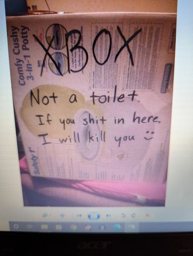 A photo taken of a laptop screen with a picture of an Xbox packed into an old Safety 1st brand training toilet. Scrawled in permanent marker: "XBOX. Not a toilet. If you shit in here, I will kill you :)"