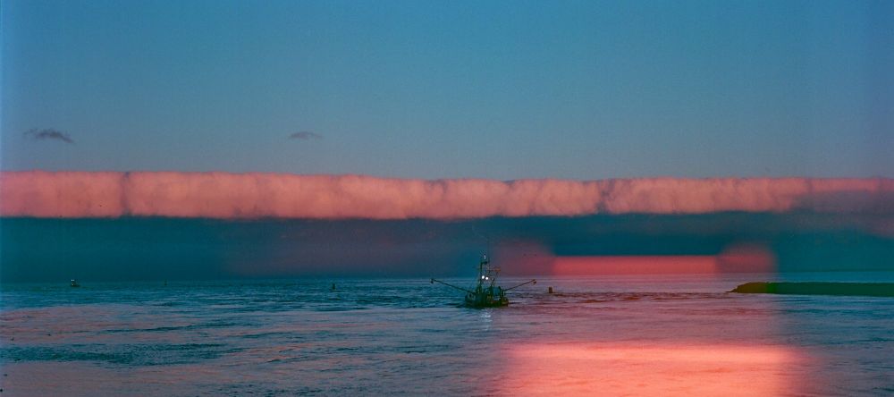 A fishing trawler headed out to sea towards a cloud wall at sunset.