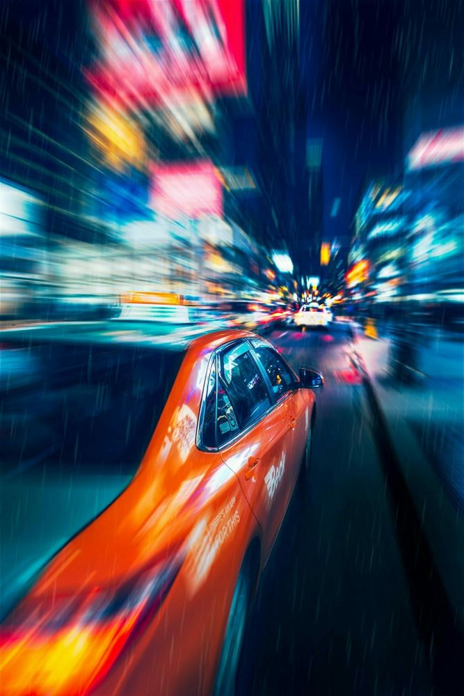 A blurred photo of a red car in a neon cityscape at night.