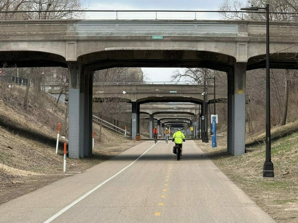 View of the Midtown Greenway looking west from 16th Ave into the tunnel of bridges with a few people biking.