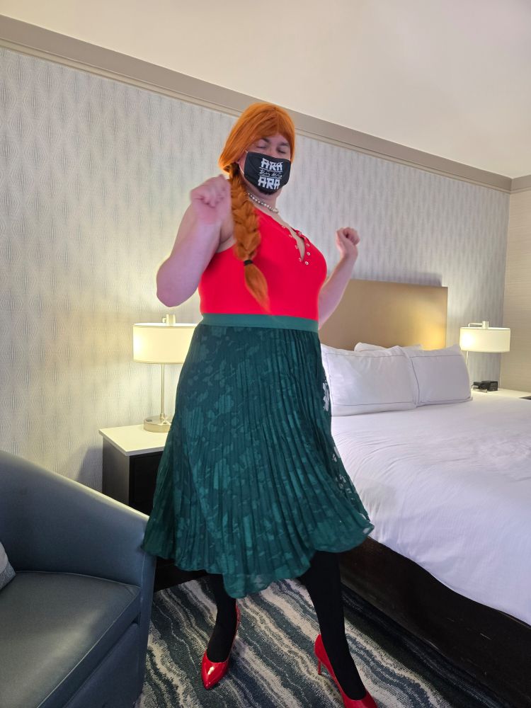 Corinne is swishing a green skirt back and forth. Red top, black tights, red pumps