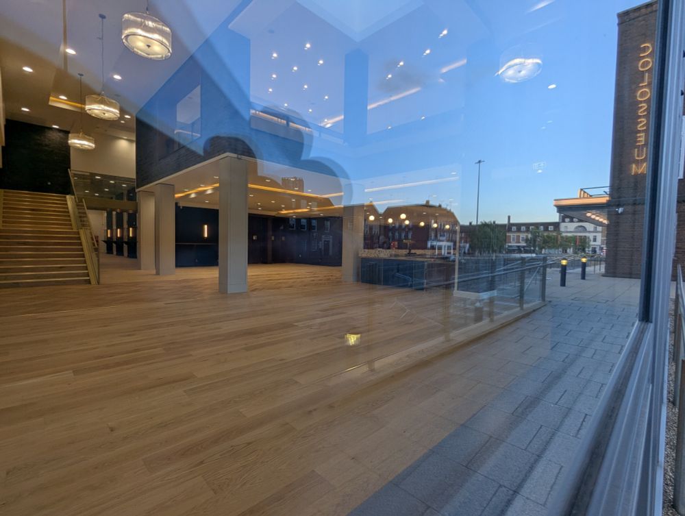 A view through the window into the cafe/bar area. The space is devoid of furniture. The floor is wooden, brand new & immaculate. Pump handles for beers can be seen on the bar on the inside.