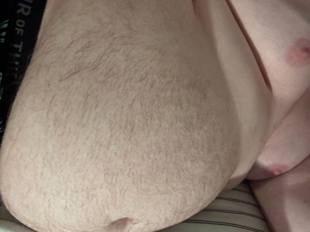 @bonniebilad’s very bloated, fuzzy vore belly, sticking well out from their body. A fat roll sits above it, much closer to the body. Both of their breasts spread out above that, with brightly pink nipples. They are splayed out on a sheet, awaiting more prey. The band of their underwear is visible, and taught against their gut. The lighting is a pale warm tone on their pale skin.