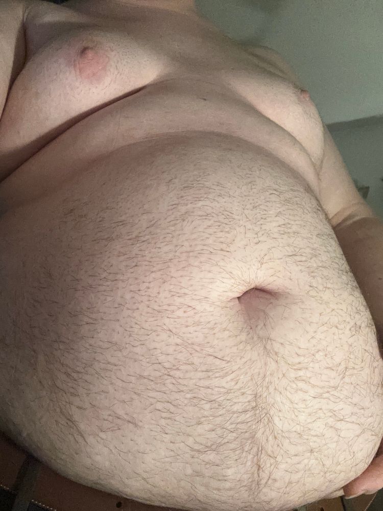@bonniebilad’s bulging fuzz-covered gut, with a roll of fat and tjeir tits sticking out above it. Their gut is filled with the remnant’s of Vore Day prey-snacks! The lighting is a warm white on their pale skin.