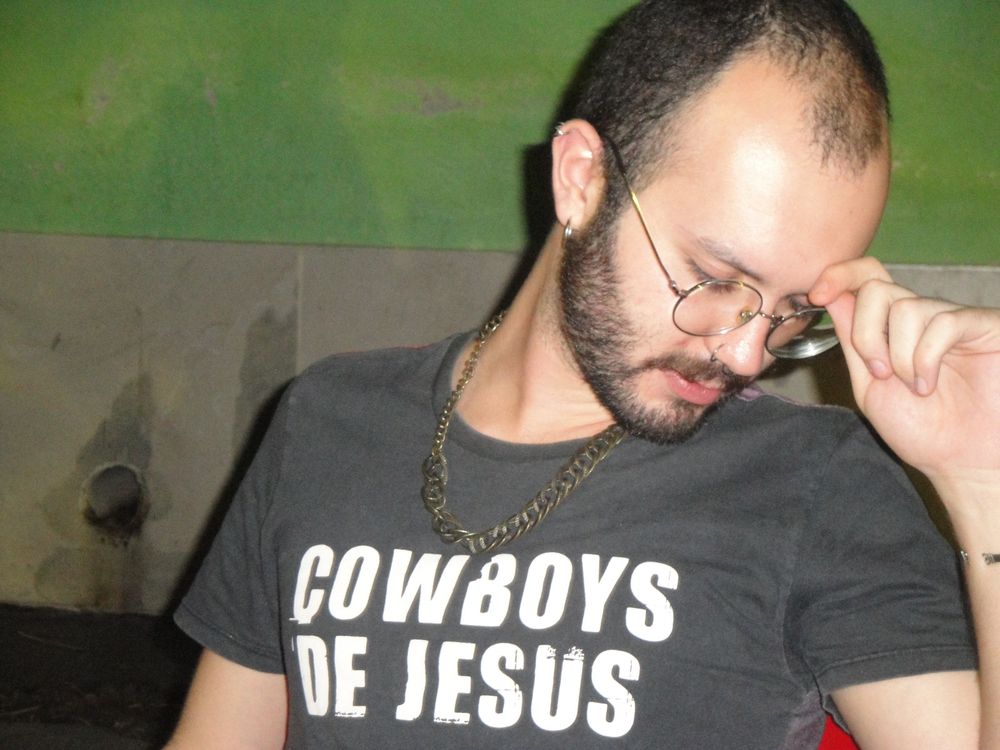 eu, um homem branco de cabelo raspado, oculos, barba e bigode, segurando a aba de um chapeu imaginário usando uma camiseta em que se lê "cowboys de jesus"