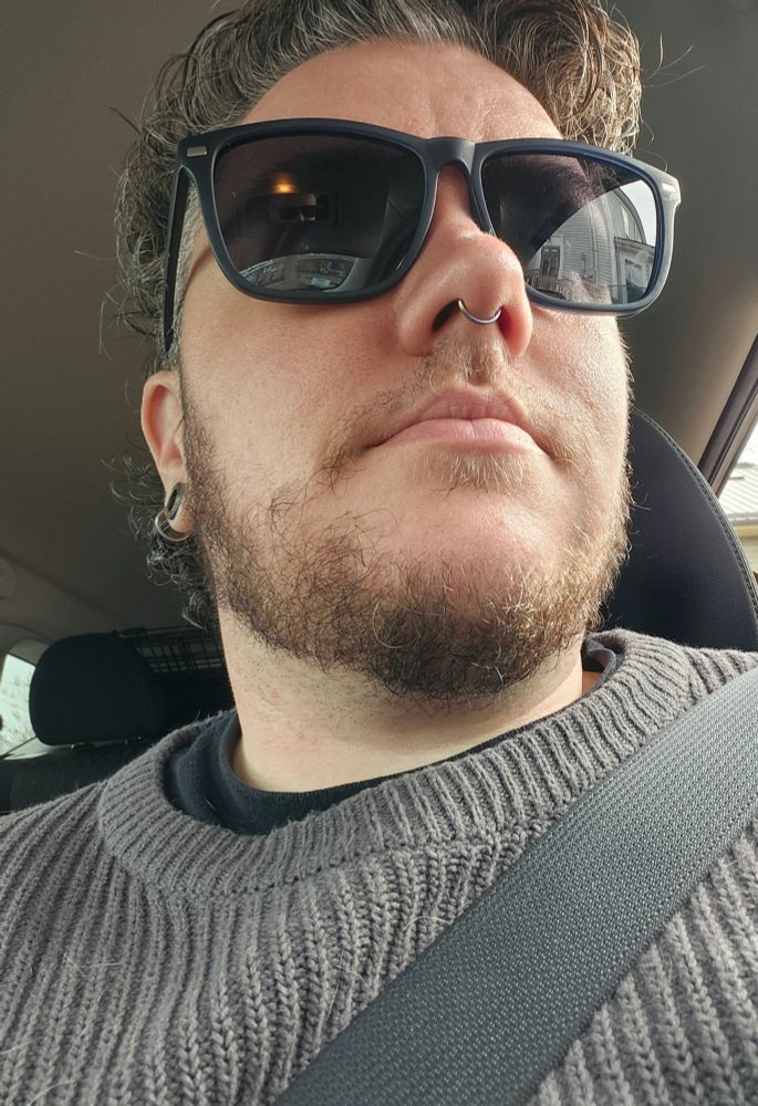 Selfie of Alfie in the car looking up at his face. He's wearing a grey cable knit sweater and black sunglasses.