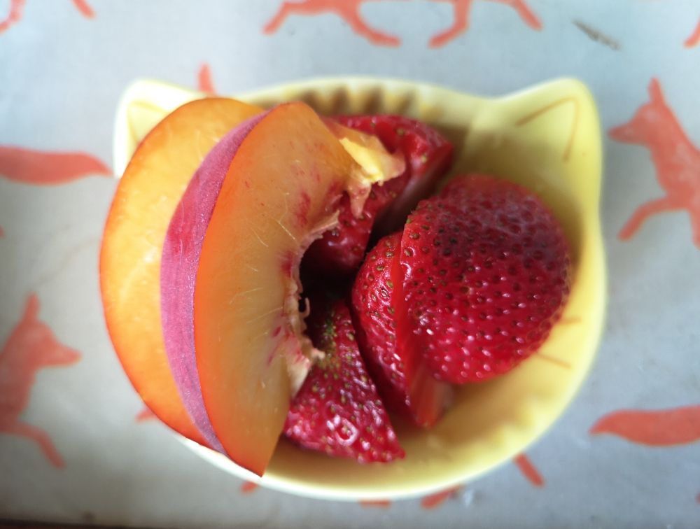 Sliced peaches and strawberries in a little cat dish on a fox print background 