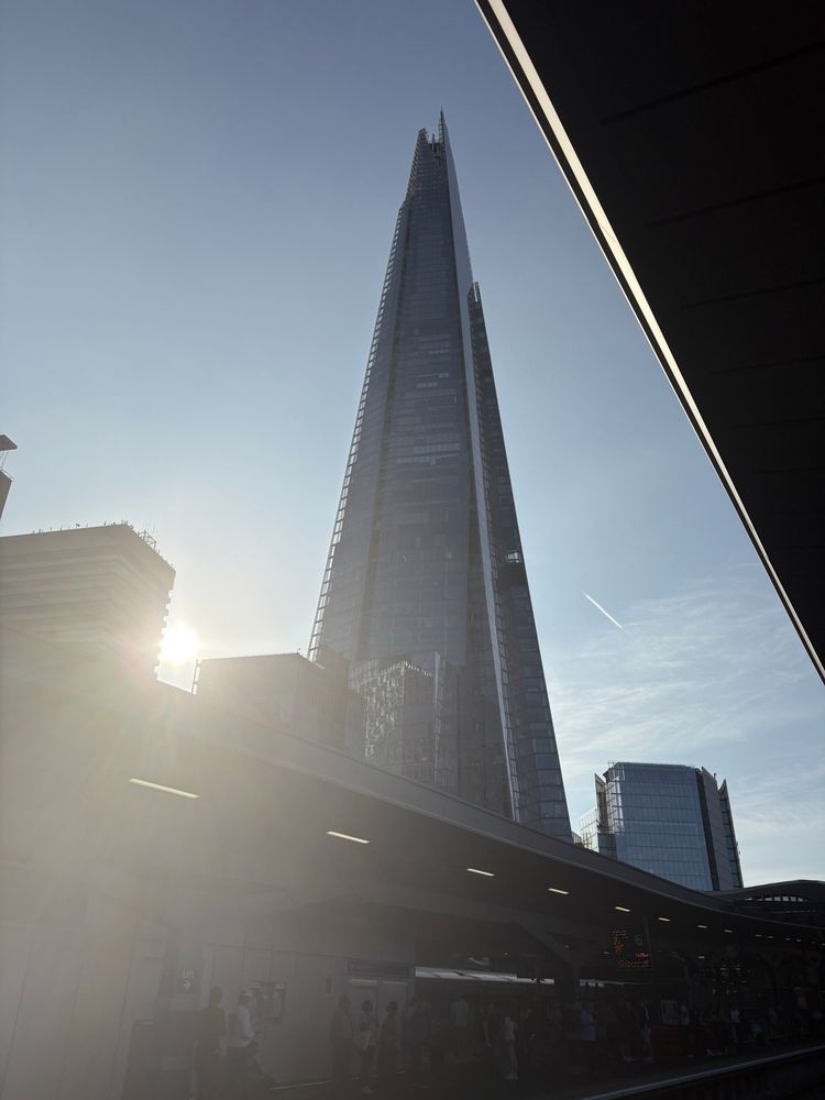 A picture of the Shard with the sun shining brightly towards the camera. The sky is blue with some high citrus and an occasional plane contrail. 