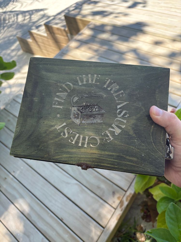 A wooden box engraved with FIND THE TREASURE CHEST on it, locked with a padlock.