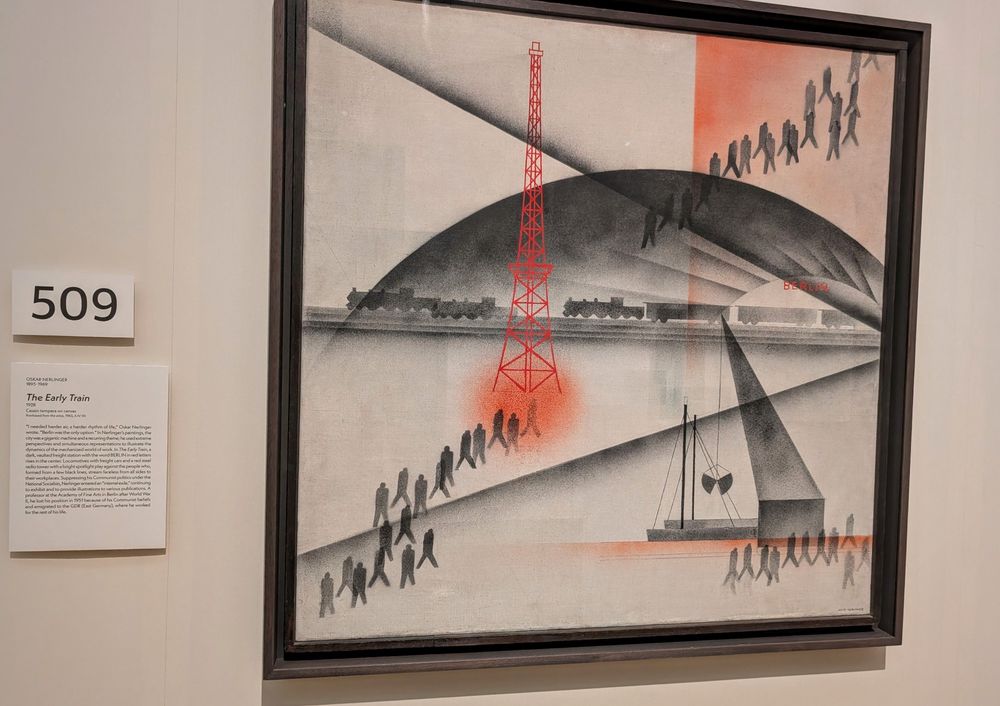 The Early Train by Oskar Nerlinger (1928)
A 1928 painting using black, white, and red to depict a regimented scene of silhouetted workers walking in diagonal lines toward a train labeled “Berlin.” A bright red radio tower dominates the center, radiating beams that divide the composition into angular sections. The stylized forms and geometric layout evoke the structure and momentum of industrial labor. Nerlinger, a committed Communist, aimed to portray “a harder rhythm of life,” reflecting the mechanized, collective experience of the working class in Weimar-era Germany. The painting emphasizes locomotion and labor, using dramatic lighting, high contrast, and minimal color to capture both the alienation and coordination of modern urban work life. The work aligns with Nerlinger’s belief that modern art must serve revolutionary goals and reflect the struggles of the proletariat.