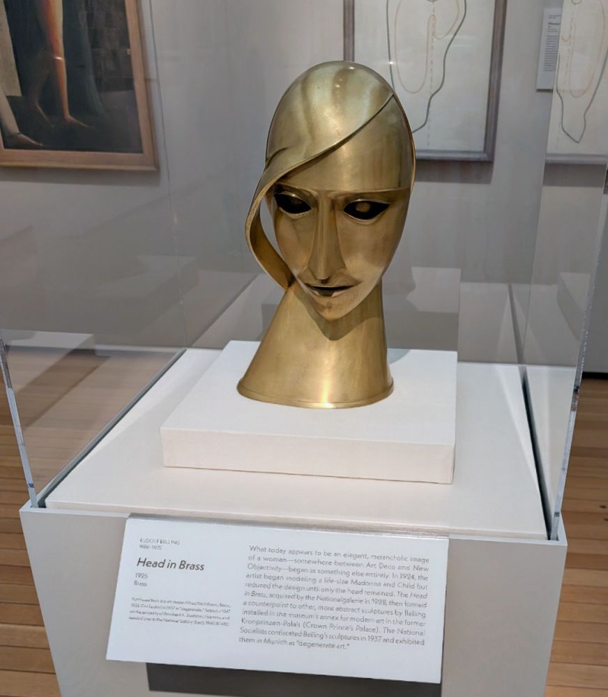 Head in Brass by Rudolf Belling (1925)

A brass bust from 1925 representing a stylized female head with simplified, geometric features and a strand of metal sweeping across the face like hair. The sculpture blends expressive form with precision, suggesting emotion within abstraction. Although it appears as a modernist symbol of elegance, the piece once sparked controversy in Weimar Germany. Critics debated whether it conveyed the spiritual essence of a human or reduced the face to pure surface and design. Belling resisted easy classification, working in a style that navigated between Expressionism and New Objectivity. The sculpture was later denounced as “degenerate art” by the Nazis, but it survived and was reintroduced to the public in 1977 by the Nationalgalerie in Berlin.