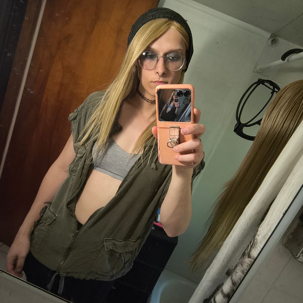 amawanth in da bathroom mirror
she's wearing black ribbed leggings, a strange, baggy green top, grey hat, black facial jewelery
black eyeshadow on top, matching green on the bottom
bra out, the shirt is unzipped most of the way 
